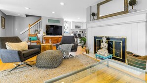 A modern living room with a fireplace, a television, and a staircase leading to an upper level. - Cloud Break (Newburyport)
