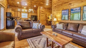 Ein rustikales Blockhaus-Interieur mit einer Küche, zwei Ledersofas, einem Holztisch und einem Kronleuchter.