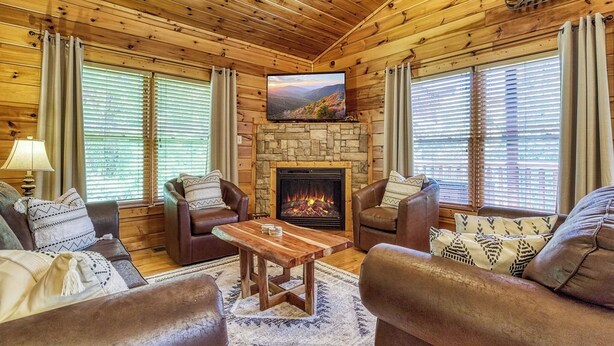 Ein gemütliches Cabin-Interieur mit Holzwänden, einem Stein-Kamin, Ledersofas und einem Fernseher, der über dem Kamin angebracht ist.
