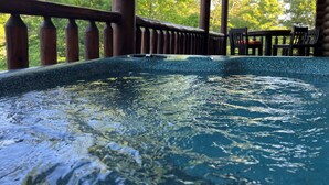 Ein Whirlpool mit einer Holzterrasse und Geländer, umgeben von Bäumen.
