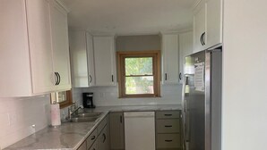 A kitchen with white cabinets, a stainless steel refrigerator, a coffee maker, and a window with a view of greenery.