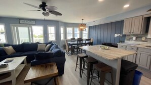 Een moderne keuken met een centraal eiland, een eetgedeelte met een tafel en stoelen, en een woonkamer met een bank en salontafel.