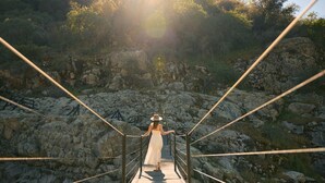 A wooden suspension bridge with metal railings, leading to a rocky landscape with trees. - Paradise Ranch Inn- Infinite House Hot Tub,Sauna. (Three Rivers)