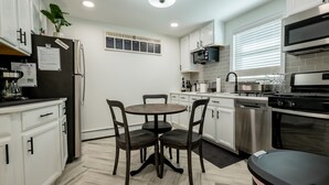 A modern kitchen with white cabinets, a stainless steel refrigerator, a dining table with chairs, and a black countertop. - Sweet and Spacious Stay Two Blocks from Wildwood's Best Beaches (Wildwood)