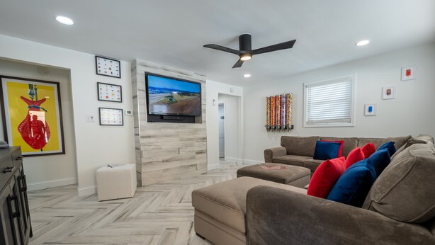 A modern living room with a large flat-screen TV, a ceiling fan, and a herringbone-patterned floor. - Sweet and Spacious Stay Two Blocks from Wildwood's Best Beaches (Wildwood)