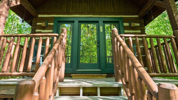A wooden cabin with a green door, a wooden staircase, and a wooden railing.