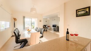 A modern living space with a dining area, kitchen, and a large window providing natural light. - 3 Bedroom Villa with Private Pool and Free Car (Paphos)