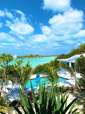 Ein Poolbereich mit klarem, blauem Wasser, umgeben von tropischer Vegetation und Blick auf den Ozean.