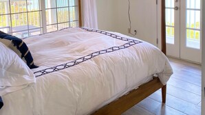 A bedroom with a ceiling fan, a bed with white bedding, a TV mounted on the wall, and a balcony with a view of the sea. - Intimate remodeled villa with private beach and pool. (Providenciales)