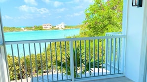 A balcony with a view of turquoise waters and buildings, wooden flooring, and a blue patterned rug. - Intimate remodeled villa with private beach and pool. (Providenciales)