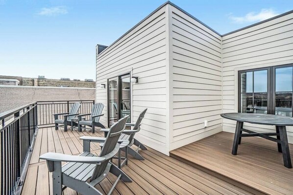 A rooftop deck with wooden flooring, a glass door entrance, and a table and chairs.