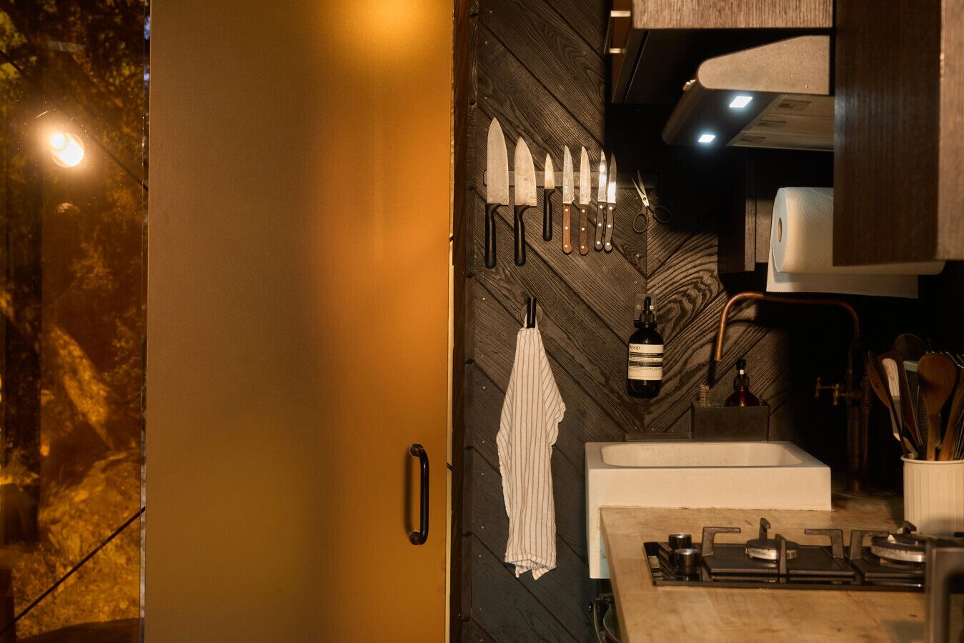A kitchen with a wooden backsplash, a sink, a stove, and various kitchen utensils.