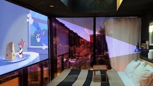 A modern hotel room with a large bed, a desk, and a TV screen displaying an animated character. - Paradise Ranch Inn- Limitless House Hot Tub,Sauna. (Three Rivers)