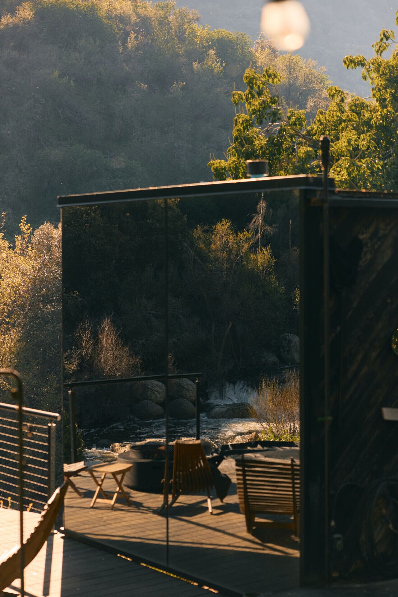 A deck with outdoor seating overlooking a rocky riverbank and forested hills.