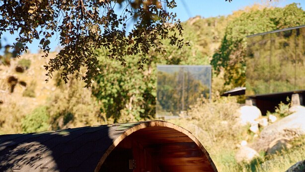 A wooden sauna with a person sitting inside, surrounded by rocks and greenery. - Paradise Ranch Inn- Limitless House Hot Tub,Sauna. (Three Rivers)