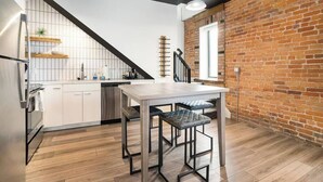 Una cocina moderna con encimera blanca, taburetes de metal negros y pared de ladrillo.