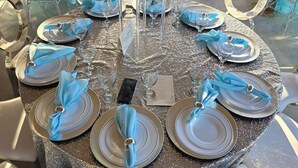 A round table set for a formal event with clear chairs, a floral centerpiece, and a smartphone on the table. - VENUE EVENTS Cbc Farms 100 person (Okeechobee)