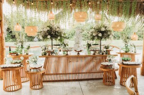 A rustic outdoor wedding setup with wooden tables, hanging lanterns, and floral arrangements.