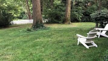 Un espace extérieur verdoyant, avec un grand arbre et deux fauteuils Adirondack.