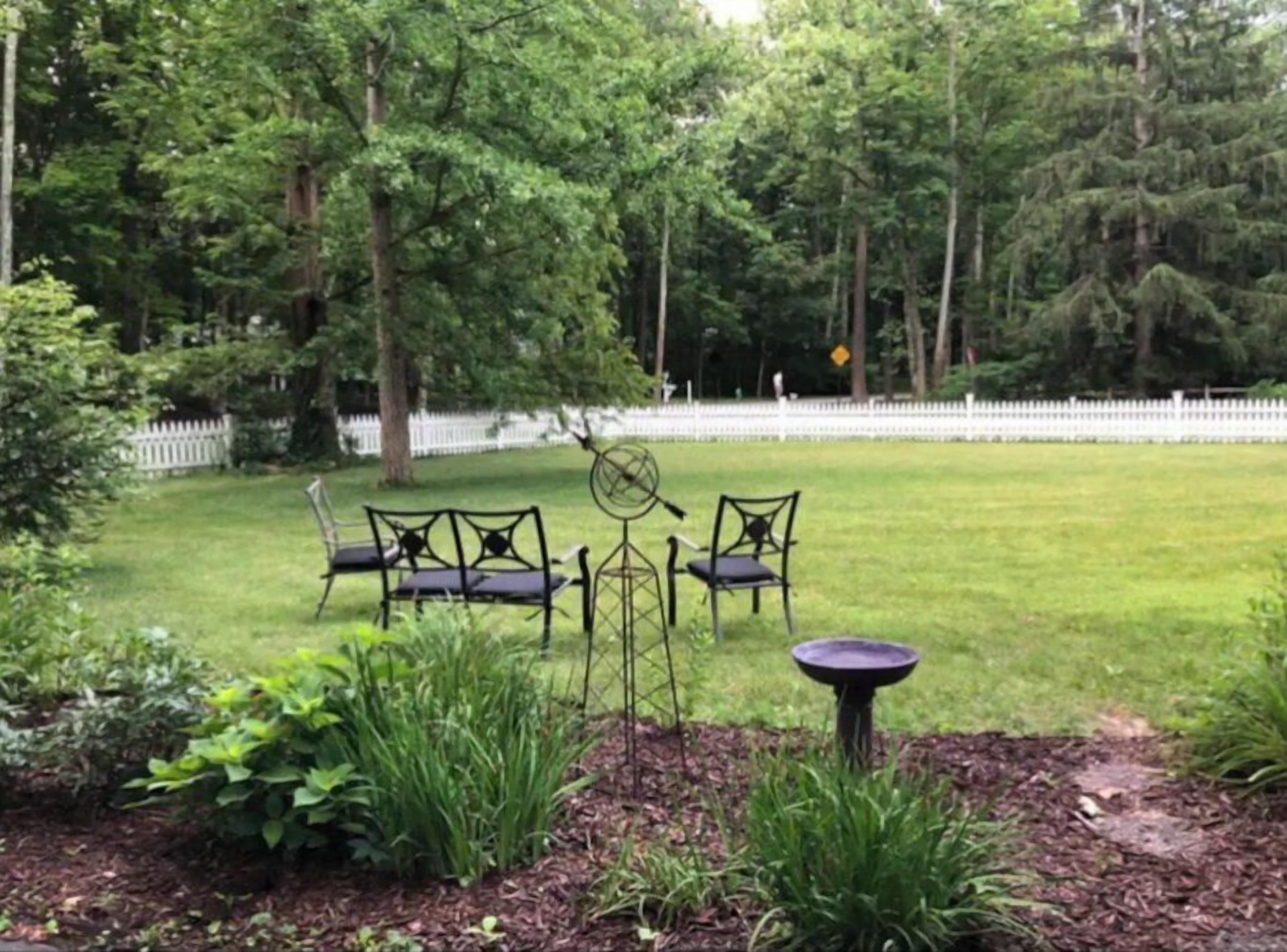 A grassy outdoor area with a white picket fence, a metal table and chairs, and a birdbath.