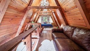 A cozy attic bedroom with a wooden ceiling, a leather sofa, and a bed with blue bedding.
