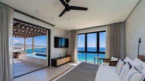 Ein modernes Hotelzimmer mit einem großen Bett, einem Deckenventilator, einem Fernseher und Blick aufs Meer.