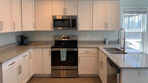 A modern kitchen with white cabinets, stainless steel appliances, granite countertops, and a view of the outside through a large window. - Newly renovated 3BR/3BA w king bed, linens, towels & views! 🌞 (Surf City)