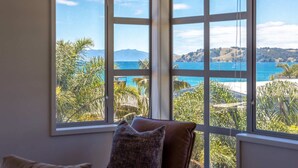 Ein Zimmer mit großem Fenster und Blick auf eine Küstenlandschaft mit Bergen und blauem Himmel.
