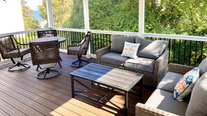 Une terrasse extérieure couverte, aménagée avec des meubles en osier, une table et un ventilateur de plafond.