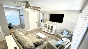 Un salon moderne comprenant un canapé, des fauteuils, une table basse, un téléviseur et un ventilateur de plafond.