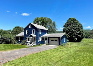 A two-story blue house with a front porch, a garage, and a well-maintained lawn.