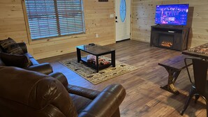 Interior acollidor d'una cabana amb un sofà de pell, una taula de cafè de vidre, una llar de foc i una televisió.
