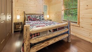 Un dormitori de cabana de fusta amb un llit, una tauleta de nit, una finestra i una porta.