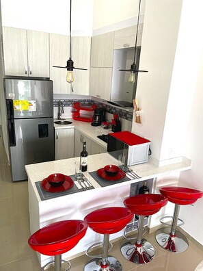 A modern kitchen with stainless steel appliances, a central island with red bar stools, and pendant lighting.