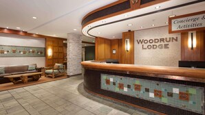 A reception area with a wooden counter, a sign for Woodrun Lodge, and a seating area with a bench and chairs. - Blackcomb Mountain condo w/ pool (Whistler)