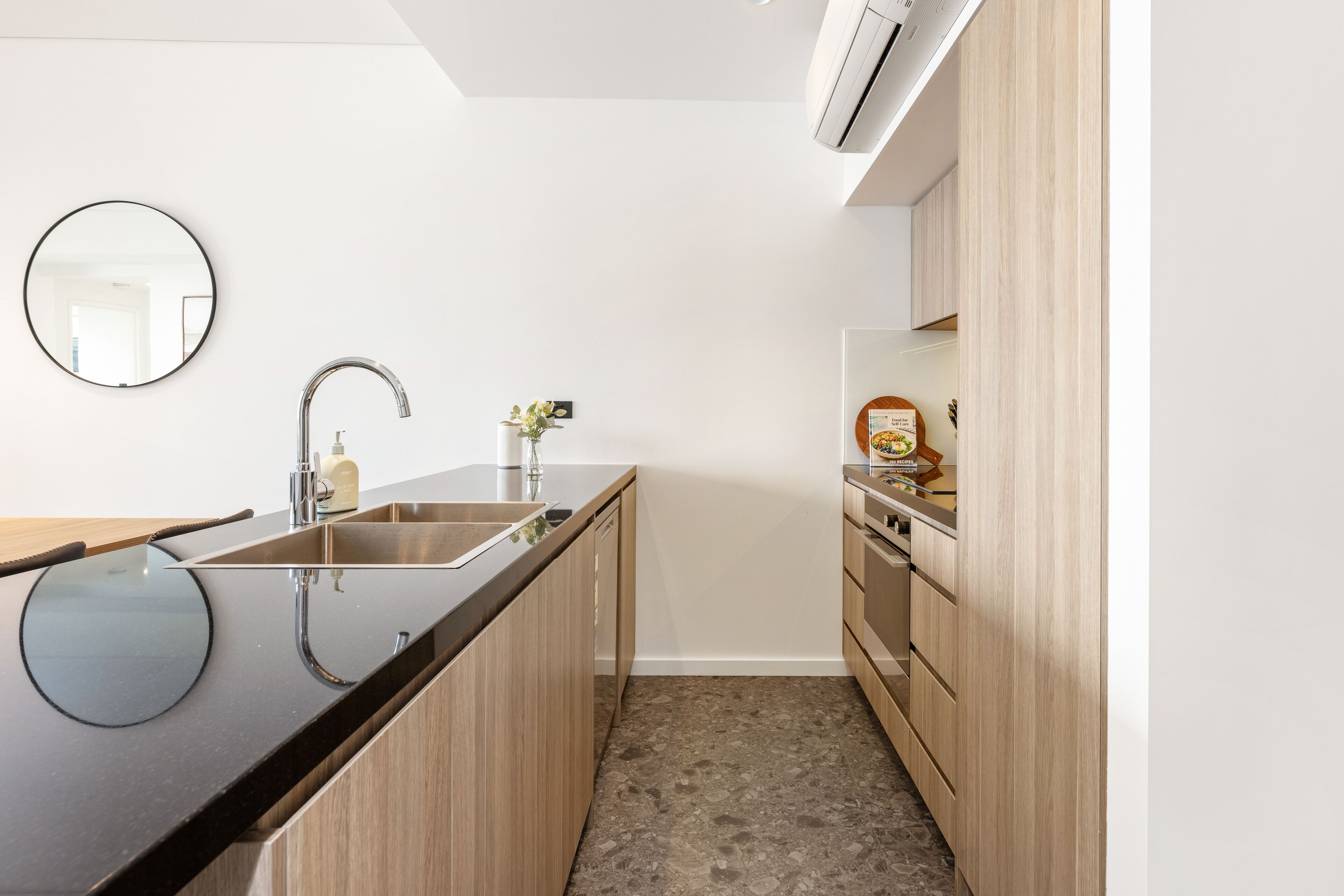 A modern kitchen with a black countertop, stainless steel sink, and wooden cabinets.
