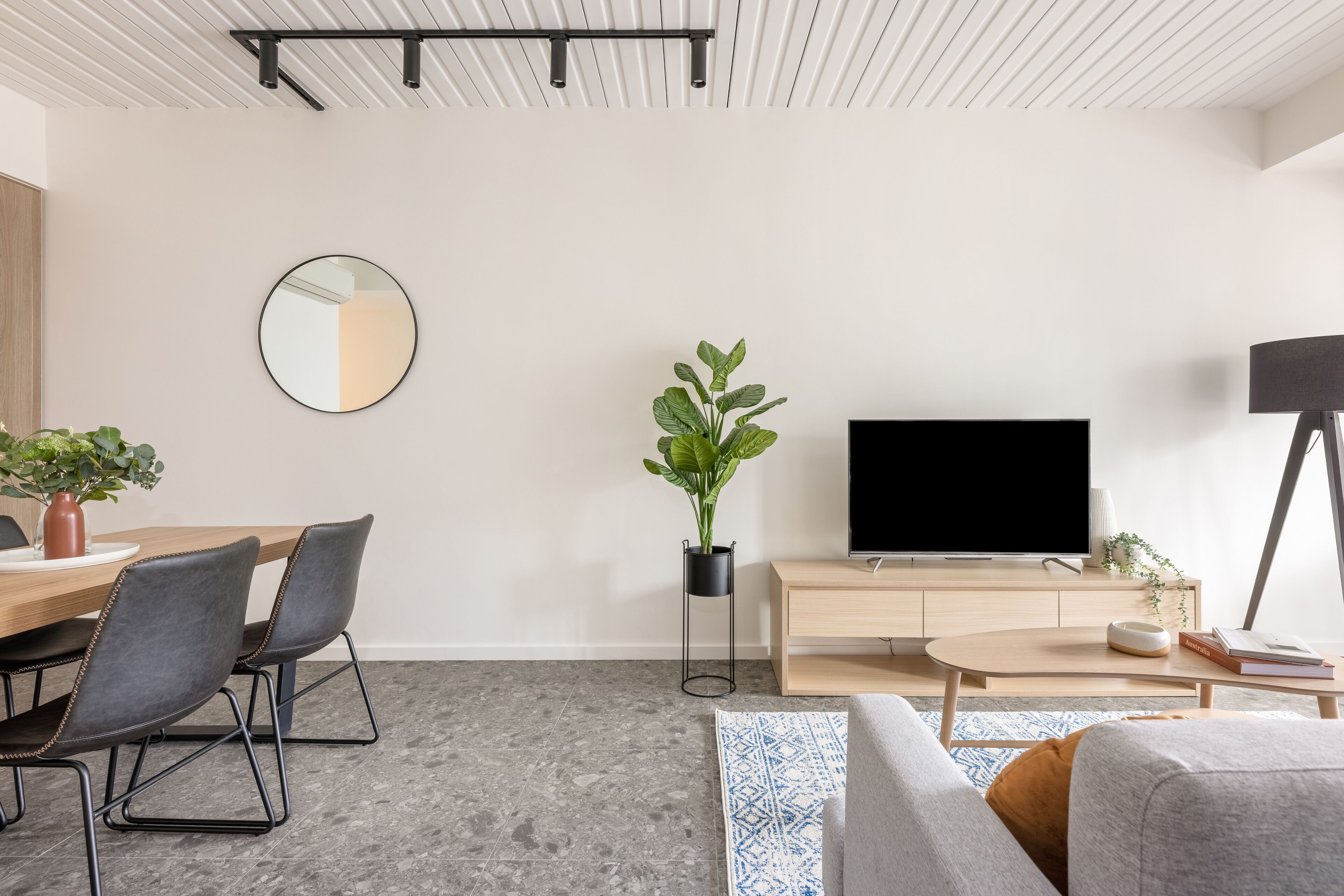 Un salon moderne avec une table à manger en bois, deux chaises, un téléviseur à écran plat, une table basse et un canapé.