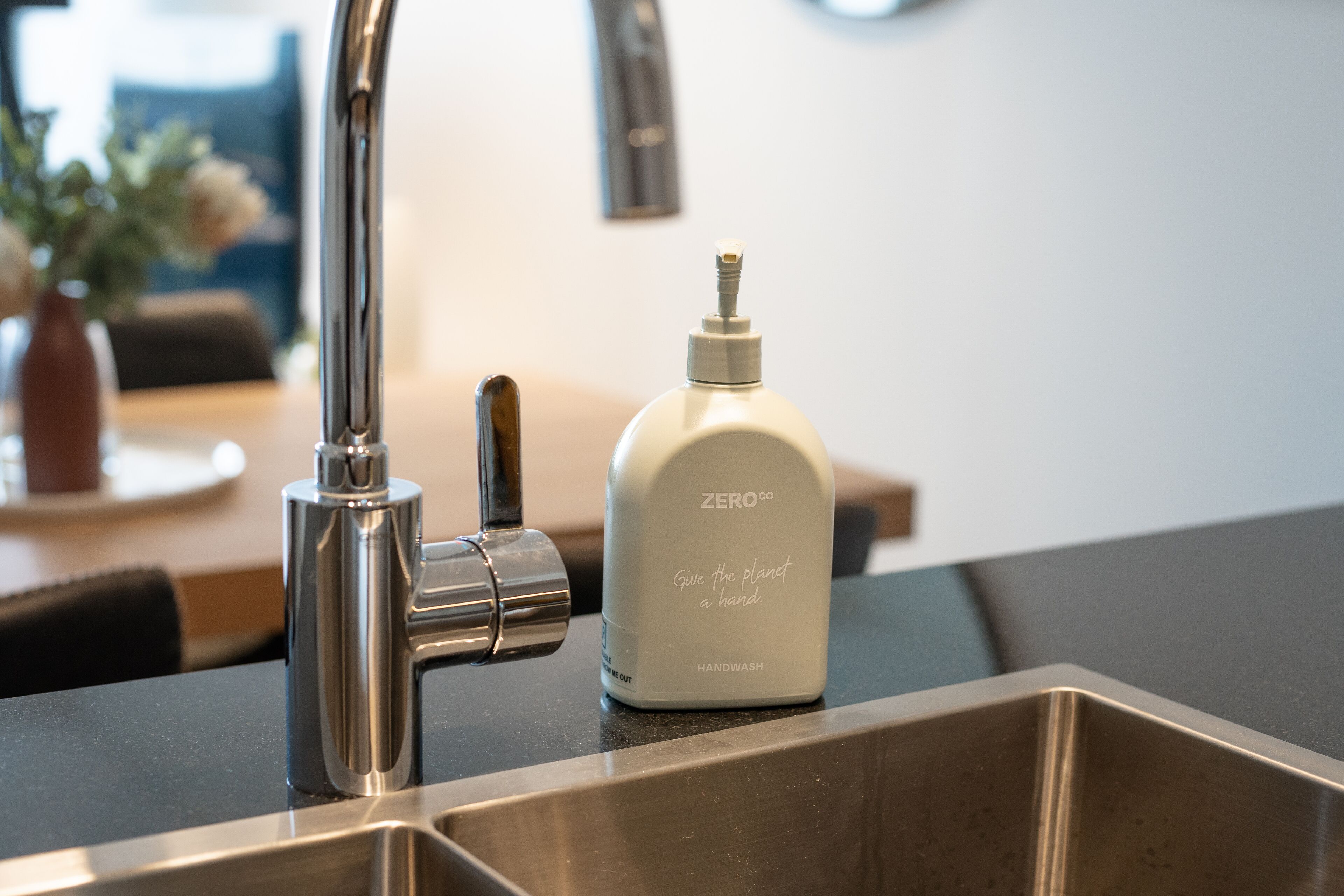 Un évier de cuisine moderne, doté d’un robinet chromé et d’un distributeur de savon blanc portant l’inscription « ZERO CO, donnez un coup de pouce à la planète ».