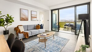 Un salon moderne avec un canapé gris, une table basse et une grande fenêtre donnant sur l’extérieur.
