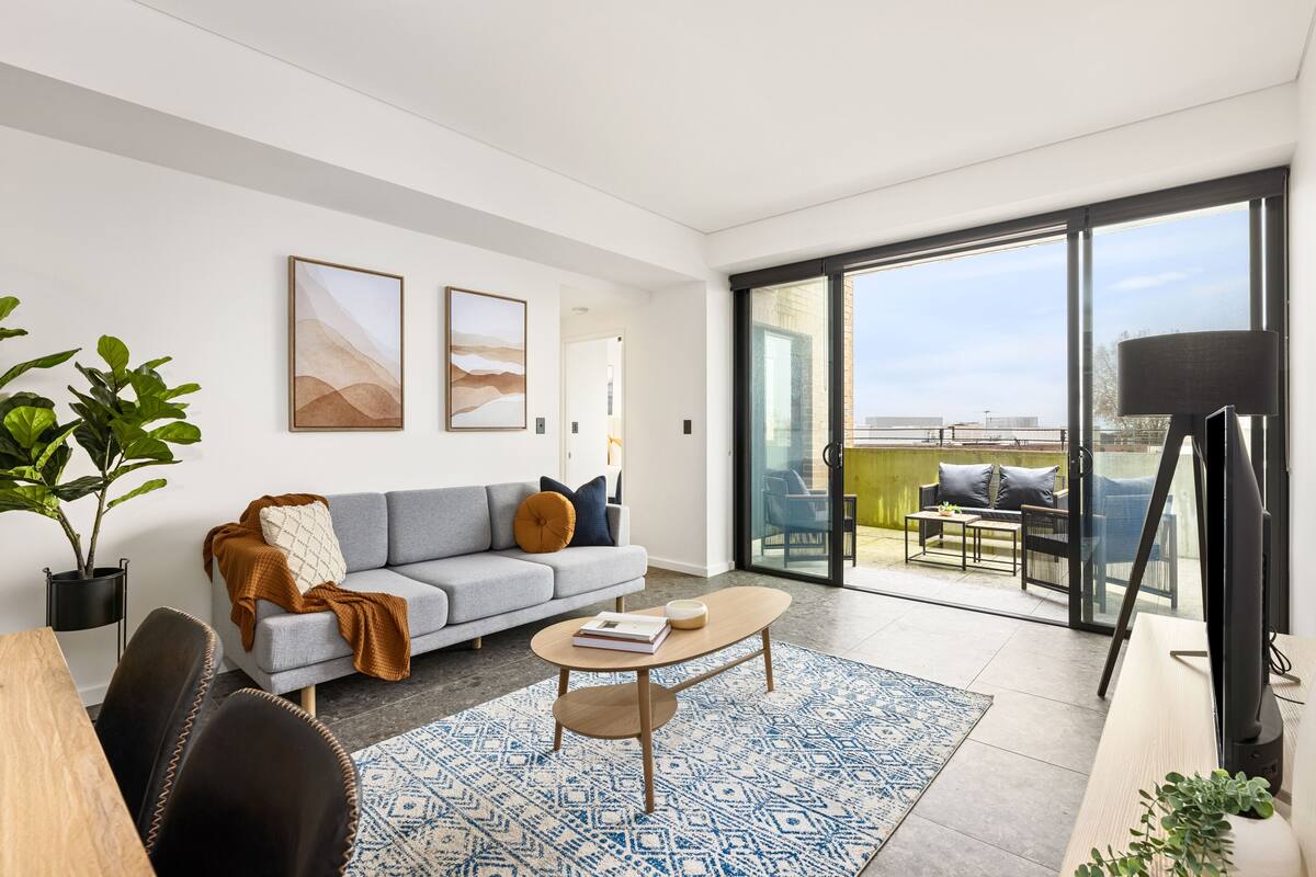 A modern living room with a grey sofa, a coffee table, and a large window offering a view of the outdoors.