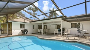 A swimming pool with a glass ceiling, surrounded by white chairs and a table, with palm trees visible outside. - ⚓Jerry's Gem! Beautiful private pool home near Anna Maria Island!⚓🌅 (Bradenton)