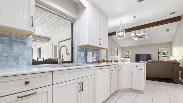 A modern kitchen with white cabinetry, a marble backsplash, and a large window. - ⚓Jerry's Gem! Beautiful private pool home near Anna Maria Island!⚓🌅 (Bradenton)