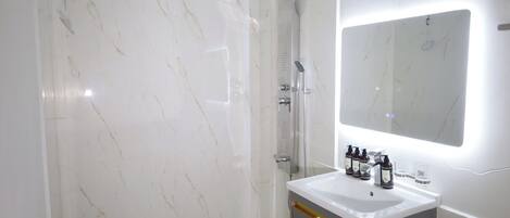 A modern bathroom with a white marble shower, a vanity with a mirror, and toiletries.