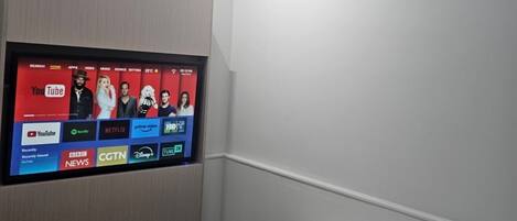 A hotel room with a flat-screen TV mounted on the wall displaying various streaming services.