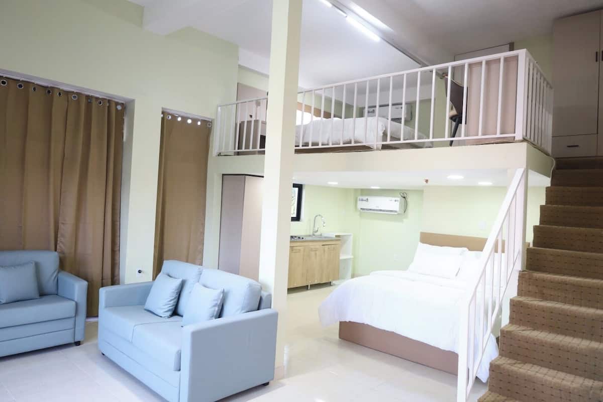 A bedroom with a bunk bed, a separate sofa, a small kitchenette, and a staircase.