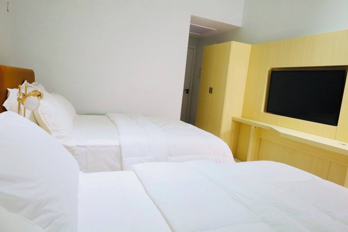 A hotel room with two beds, a TV mounted on the wall, and a wooden wardrobe.