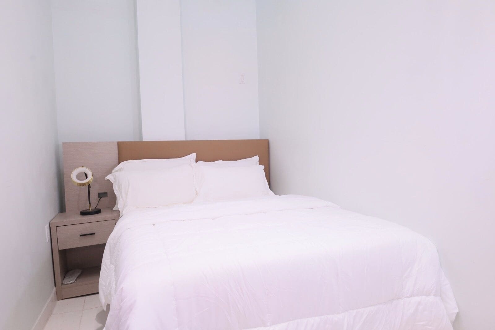 A neatly made bed with white bedding, a wooden headboard, and a bedside table with a lamp.