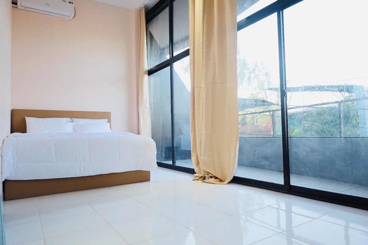 A bedroom with a bed, a window with a curtain, and a view of the outside.