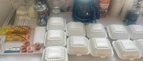 A table with food containers, condiments, and a coffee maker.