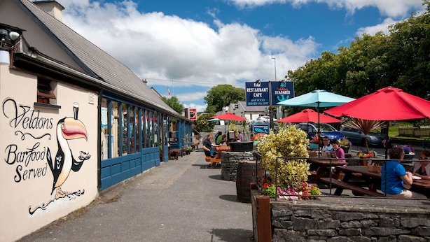 Une rue où se trouvent un restaurant de fruits de mer et un café, avec des tables en terrasse protégées par des parasols, et une fresque représentant un oiseau.
